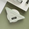 A green herringbone patterned pet bandana labeled "Cocopup London," known as the Sage Tweed Bandana, is neatly folded into a triangle and placed on a round white dish against a green background, showcasing its lightweight and breathable design. A matching country style pet accessory is visible at the top of the image.
