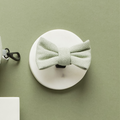 Sage green tweed dog bow tie with herringbone pattern displayed on a white stand against a green background.