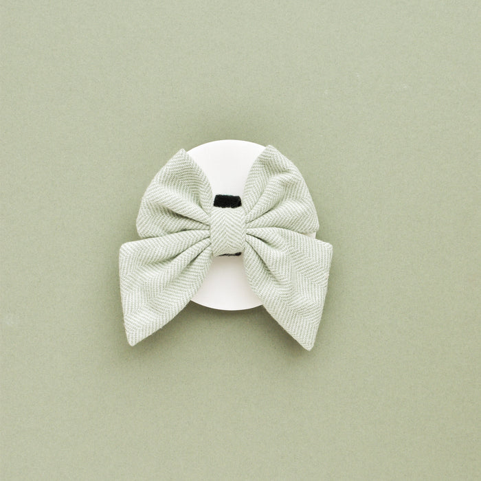 Sage tweed sailor bow tie with black center, displayed on white background and matching sage green surface.