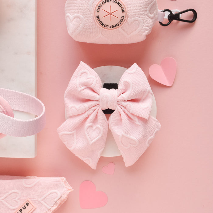 Baby pink heart-patterned sailor bow tie displayed with pink accessories and paper hearts on a pink background.