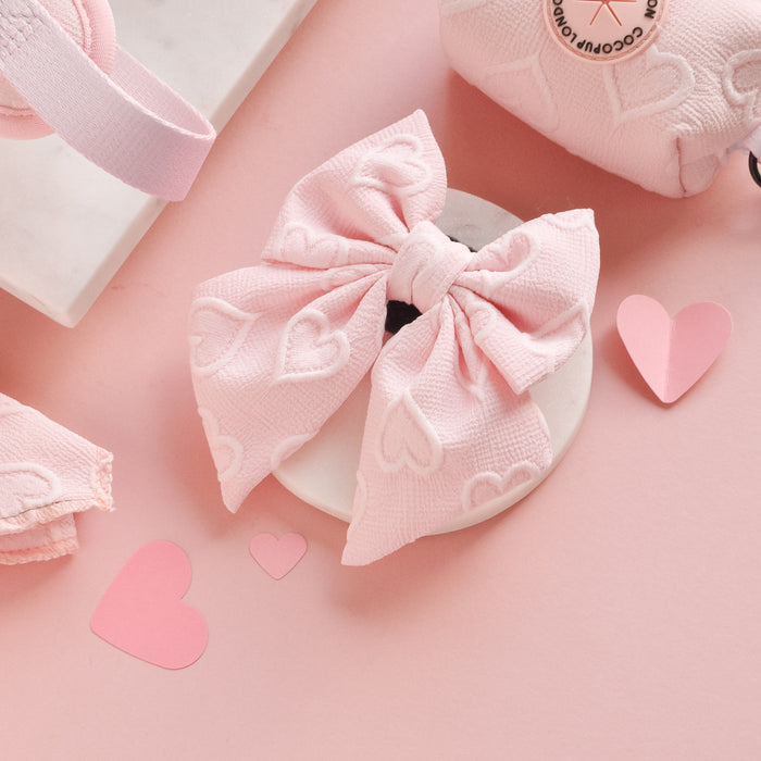 Baby pink heart-patterned Luxe Sailor Bow Tie by Cocopup London on a pastel pink background with paper hearts.