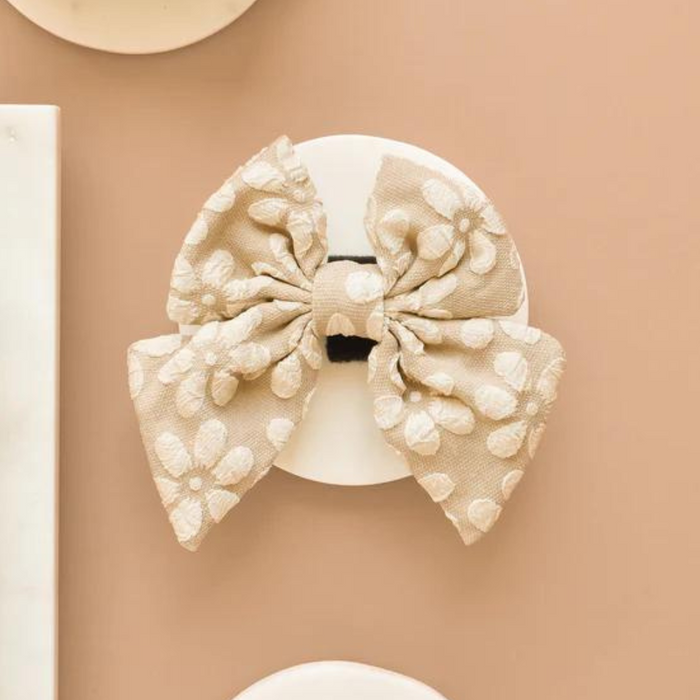 Mocha flower print sailor bow tie on a round white card, set against a beige background.