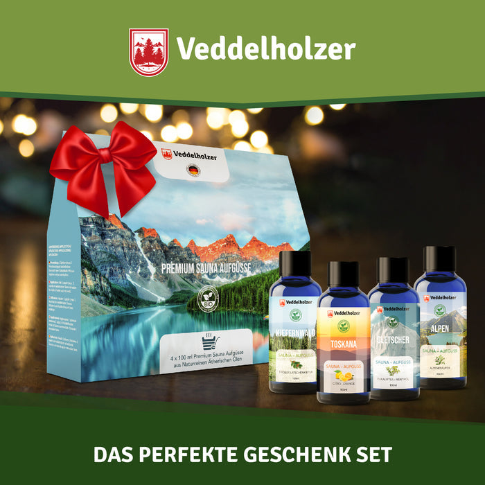 Geschenkkarton mit roter Schleife im Lichterglanz, davor die vier Flaschen – Aufdruck „4 x 100 ml Premium Sauna Aufgüsse“