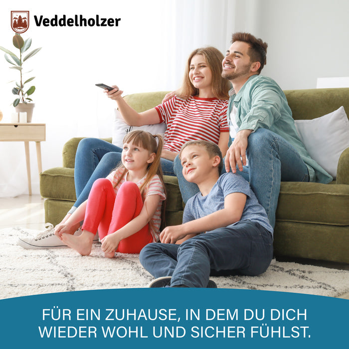 Vater, Mutter und zwei Kinder sitzen lachend vor einem grünen Sofa im hellen Wohnzimmer, die Mutter hält die Fernbedienung