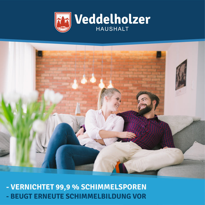 Paar sitzt eng nebeneinander auf einem grauen Sofa vor einer Backsteinwand, im Vordergrund weiße Tulpen