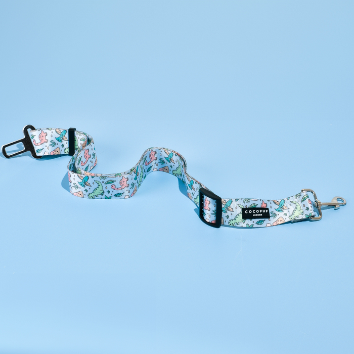 Cocopup London seat belt restraint featuring a playful Dinopaws print with cartoon dinosaurs on a green background.