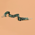 Khaki leopard print seat belt restraint with metal clips on a peach background.