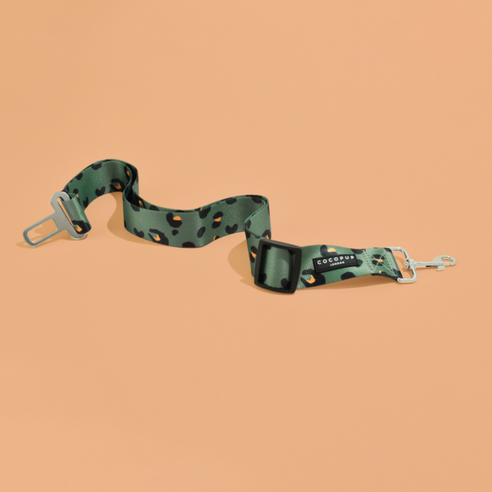 Khaki leopard print seat belt restraint with metal clips on a peach background.