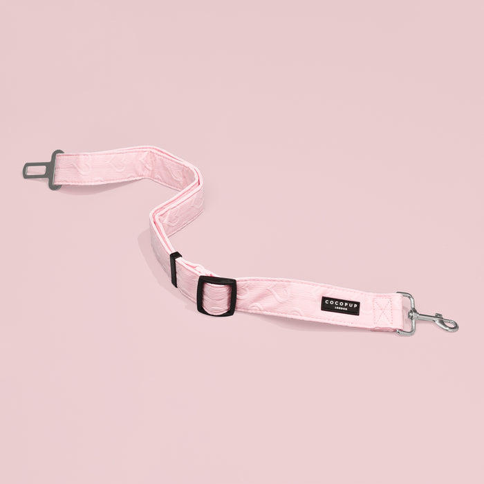 Pink heart-patterned Cocopup London seat belt restraint with metal clips and adjustable strap on a pink background.