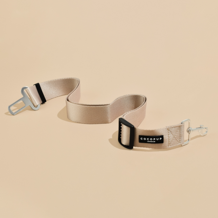 Plain nude Cocopup London seat belt restraint with metal clips on a beige background.