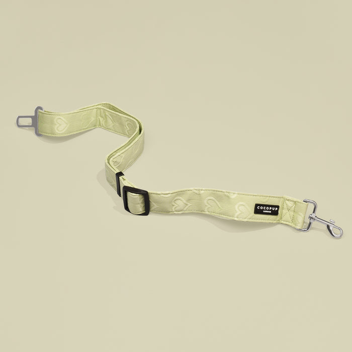 Sage green seat belt restraint with heart patterns, displayed on a light beige background.