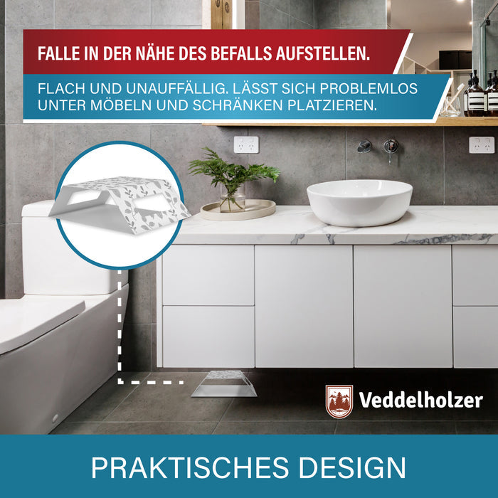 Falle steht flach neben dem Unterschrank im grauen Bad, eine Lupe zeigt die niedrige Bauform der Klebefalle