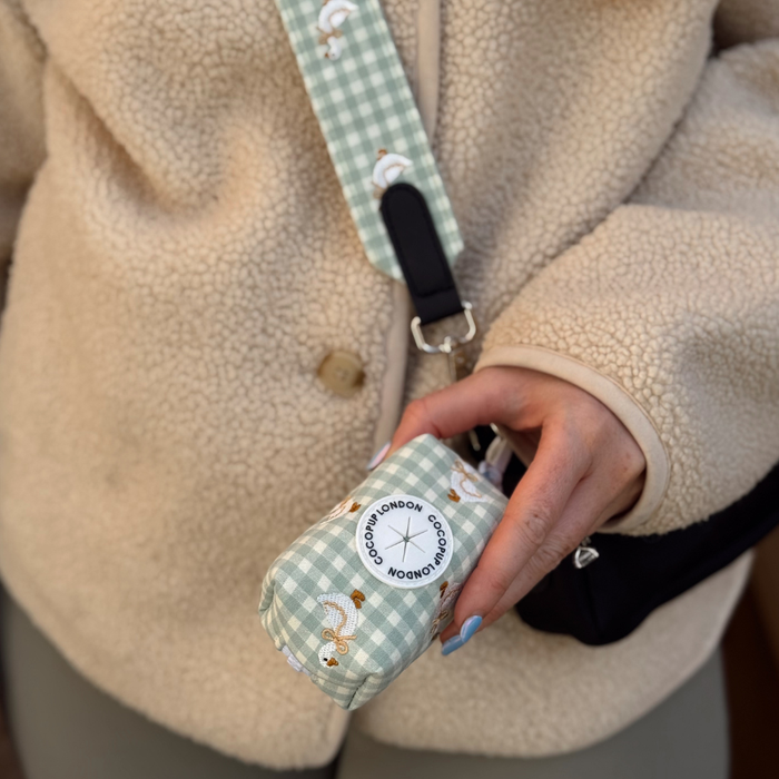 Sage green gingham and floral poop bag holder by Cocopup London held by a person in a beige fleece.