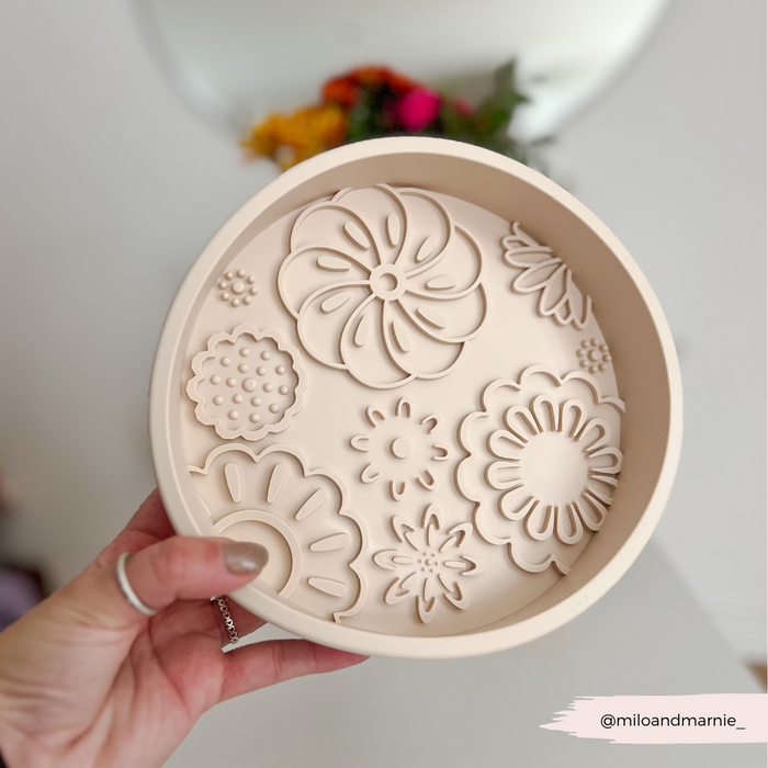 Hand holding a pink floral-patterned Cocopup London slow feeder dog bowl; blurred flowers in background.