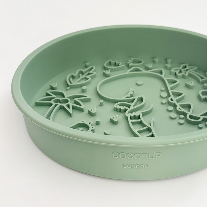 Green silicone slow feeder dog bowl mat shaped like a dinosaur with palm tree accents.