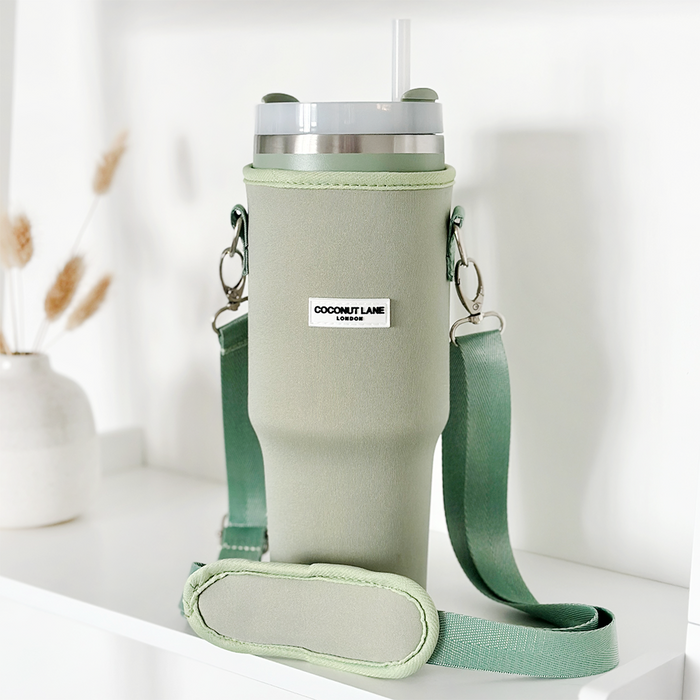 Soft sage tumbler carry case with strap and straw, displayed on a shelf next to a simple vase.