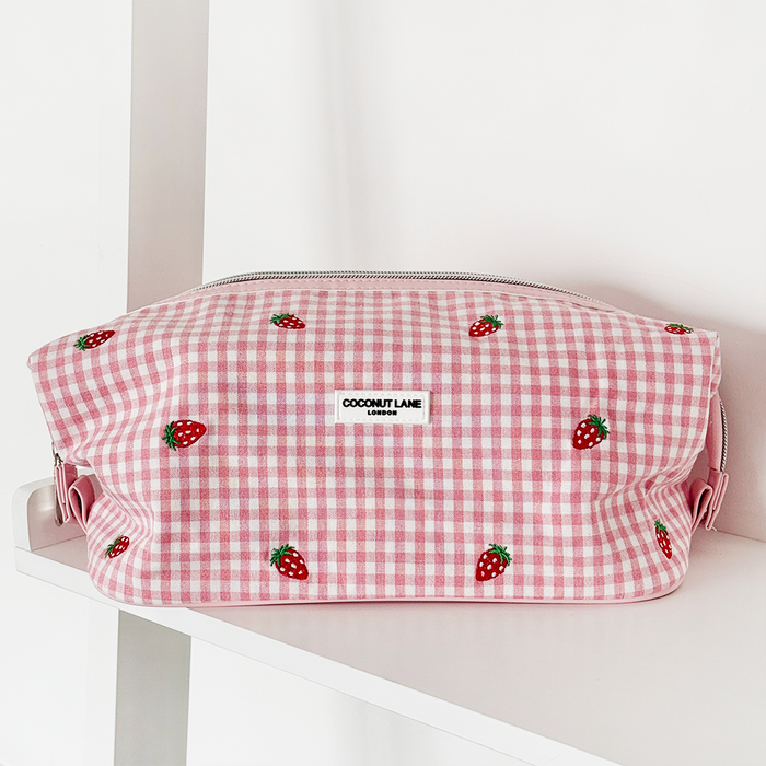 Strawberry-patterned expandable makeup bag with Coconut Lane label displayed on a white shelf.