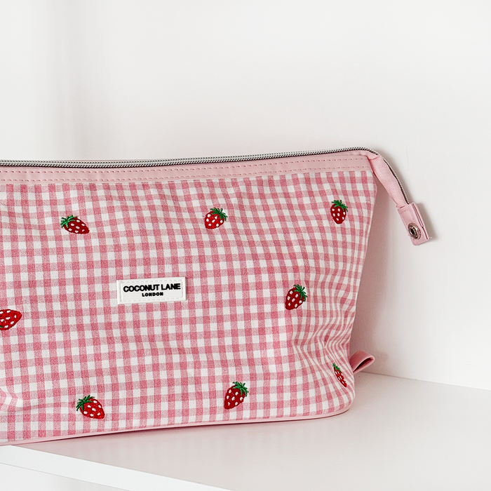 Pink Strawberry Picnic print makeup bag with green leaves sits on a white shelf.