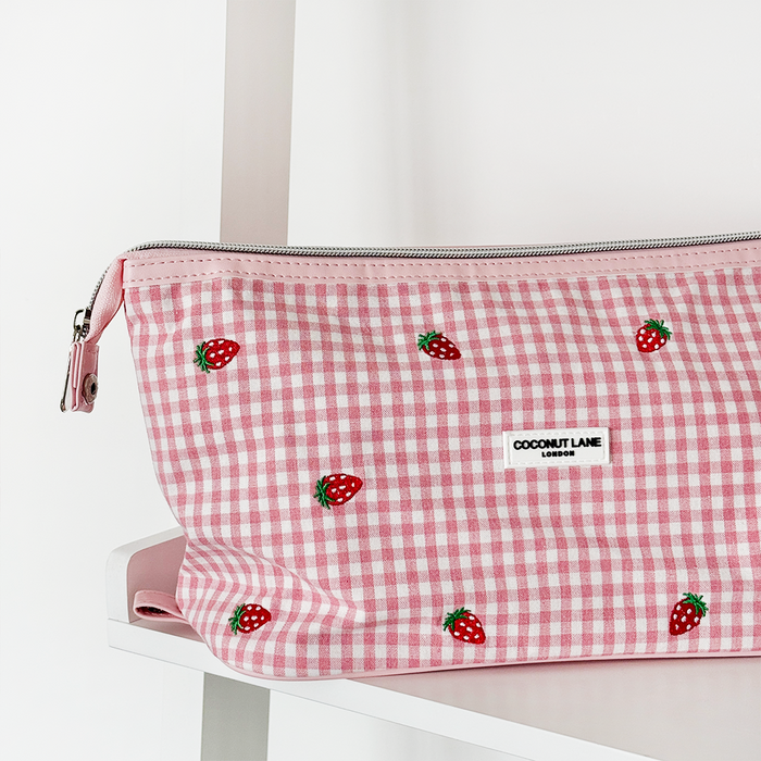 Pink Strawberry Picnic expandable makeup bag with strawberry pattern, displayed on a white shelf.