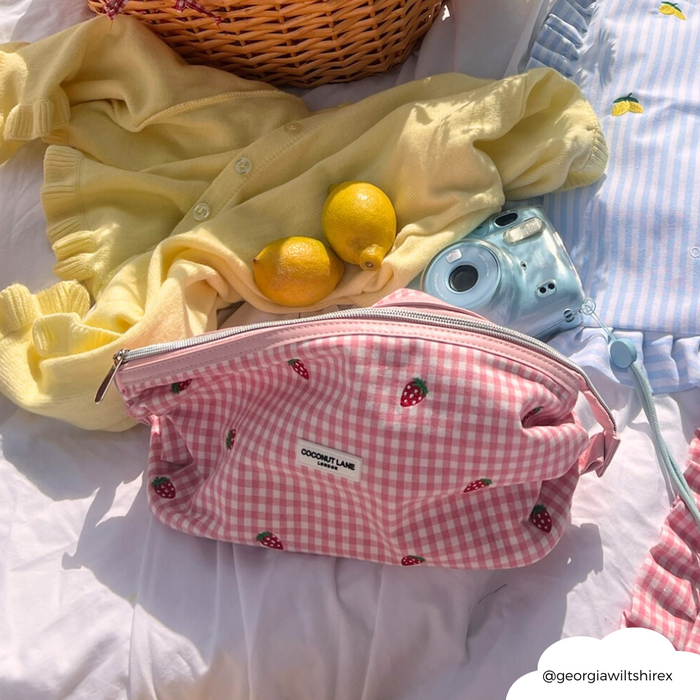 Strawberry Picnic expandable makeup bag with pink strawberry pattern, shown on a picnic blanket with lemons and a blue camera.