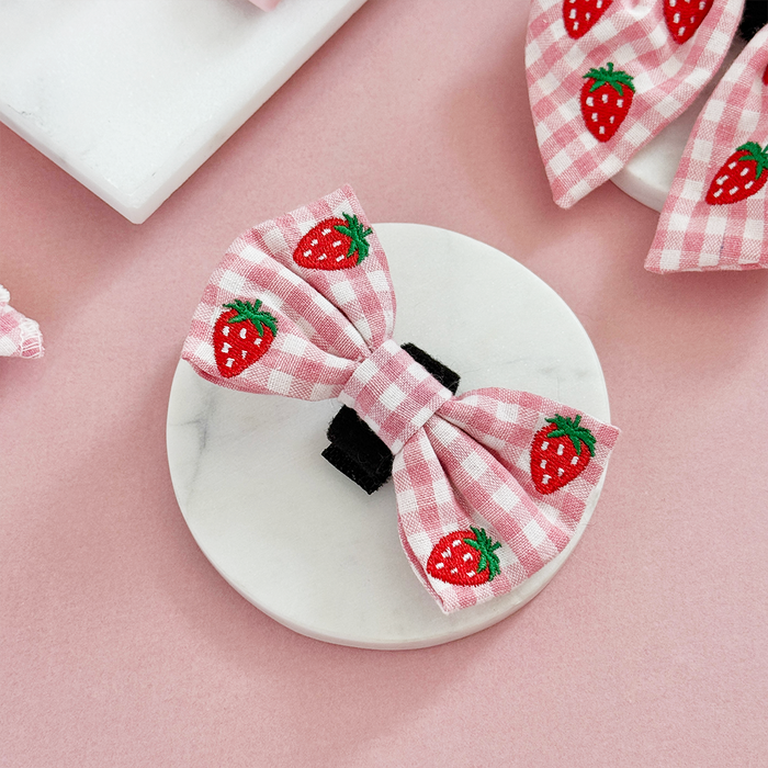 Strawberry-embroidered Cocopup London bow tie on a marble dish with a pink background.