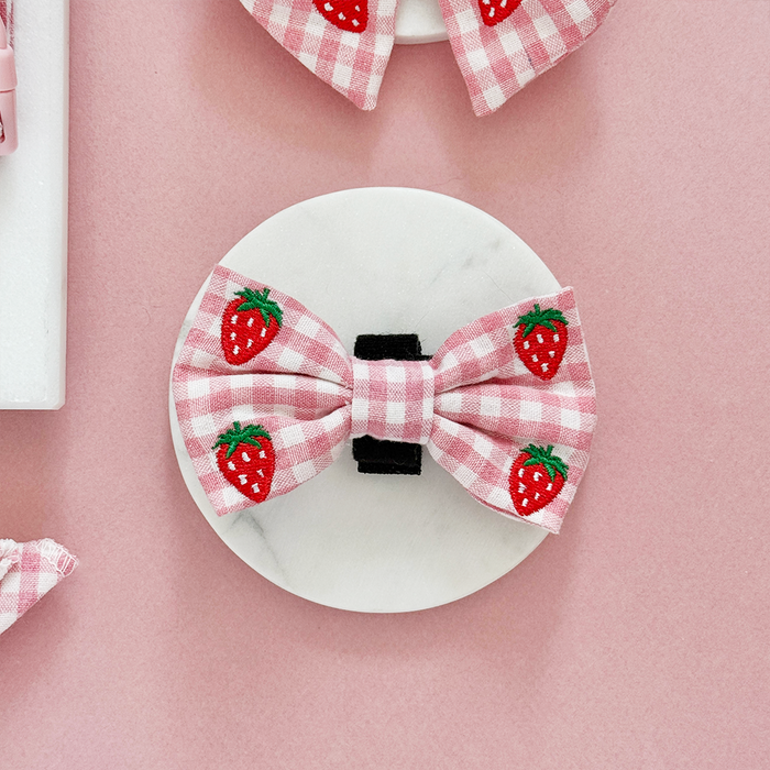 Cocopup London pink bow tie with strawberry print on white marble, set against a pink background.