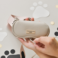 Hand holding a beige dog walking bag next to a caramel Cocopup London sunglasses case with paw prints.