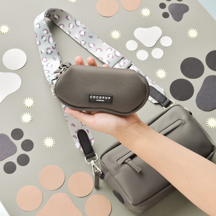 Grey dog walking bag with leopard strap held in hand, shown beside a matching bag and mocha sunglasses case.