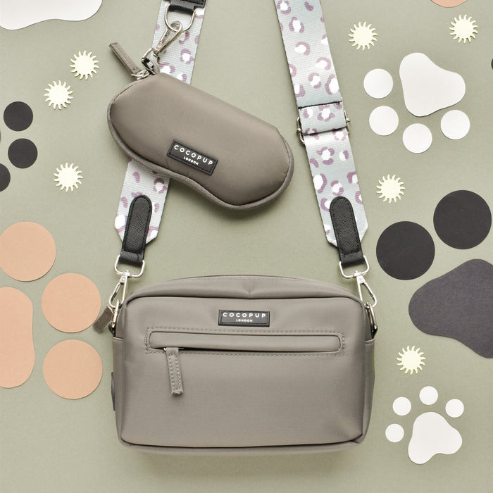 Grey dog walking bag with leopard print strap and paw prints, shown beside a brown sunglasses case.