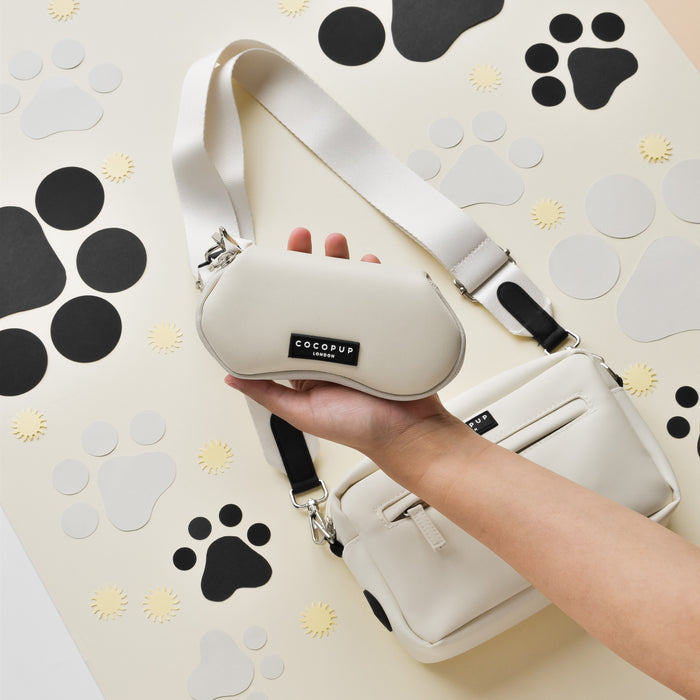 Cream Cocopup London sunglasses cases, one held in hand and one on a surface with a paw-print pattern.