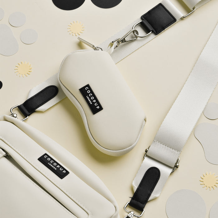 Oyster white and cream dog walking bag with strap, next to a Cocopup London sunglasses case on a beige patterned background.
