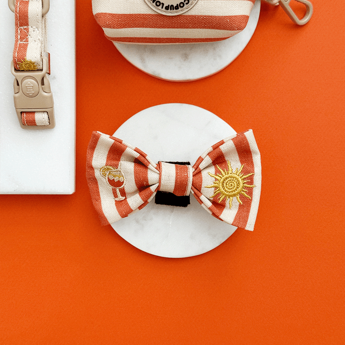 A orange and beige stripe dog bow tie, with embroidered drink and sun graphics.
