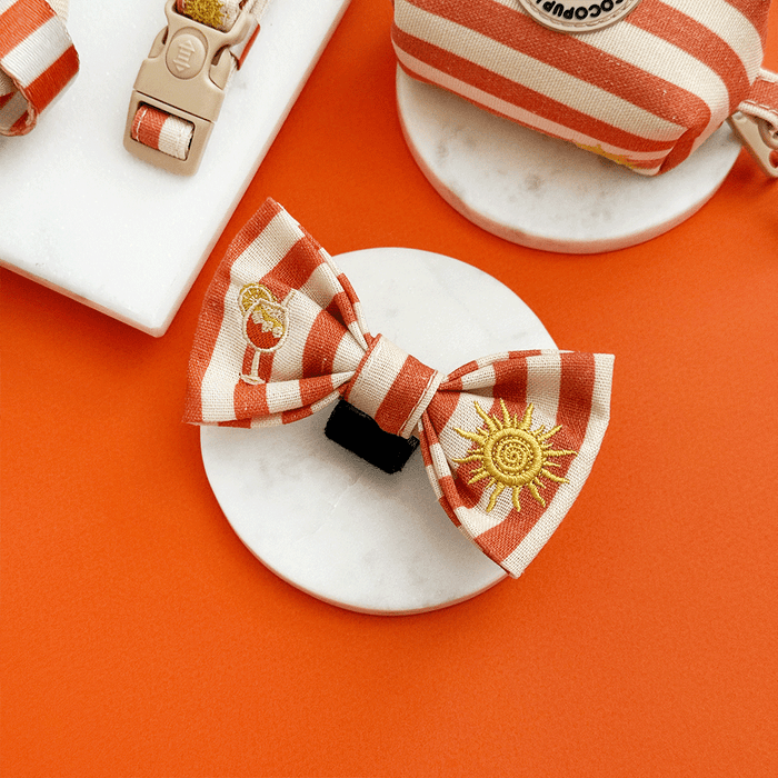 A orange and beige stripe dog bow tie, with embroidered drink and sun graphics.