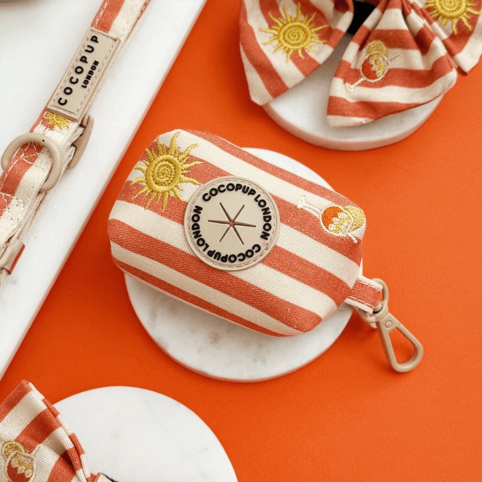 A orange and beige stripe poop bag holder, to hold dog poo bags, with embroidered drink and sun graphics.
