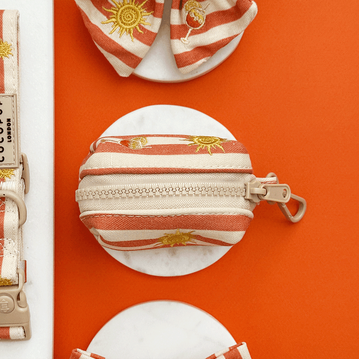 A orange and beige stripe poop bag holder, to hold dog poo bags, with embroidered drink and sun graphics.