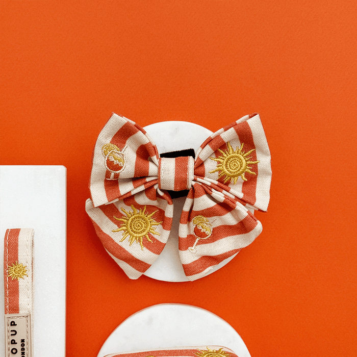 A orange and beige stripe dog sailor bow tie, with embroidered drink and sun graphics.