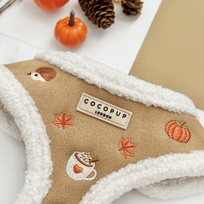 Brown dog harness with white sherpa trim and autumnal-themed embroidery of pumpkins, leaves, a coffee cup, and mushrooms.
