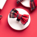 Red tartan bow tie hair clip by Cocopup London on a white stand, set against a red background.