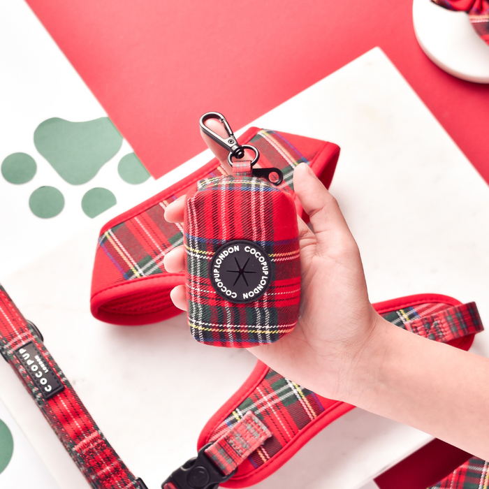 Hand holding a tartan Cocopup London poop bag holder with clip, next to matching accessories on a white surface.