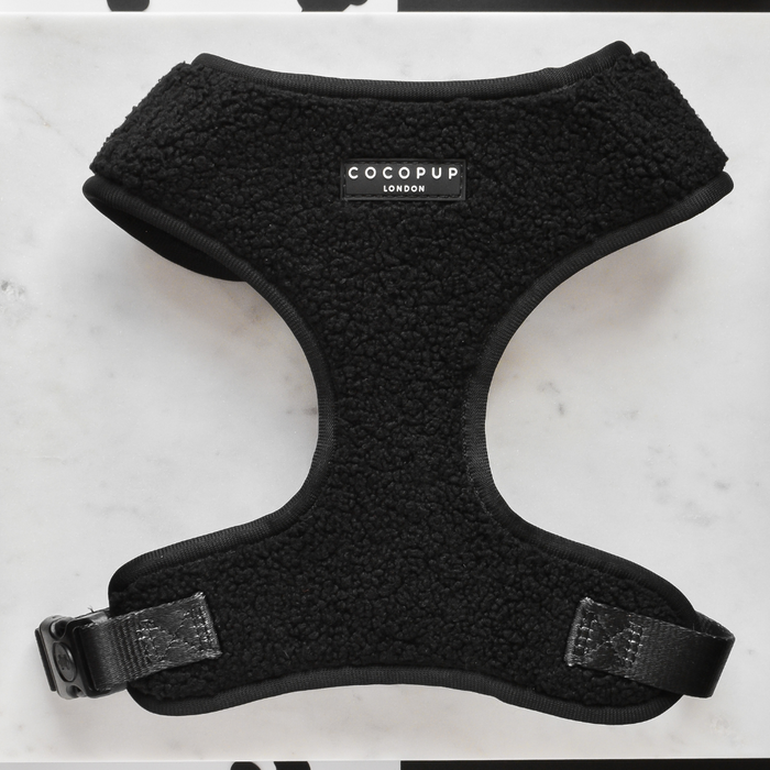A black, fleece-lined dog harness labeled "Cocopup London" lies flat on a white surface. This Teddy Adjustable Neck Harness - Baloo features a sturdy black buckle for fastening and reinforced stitching for durability, perfect for any dog walk with its teddy soft material.