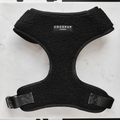 A black, fleece-lined dog harness labeled "Cocopup London" lies flat on a white surface. This Teddy Adjustable Neck Harness - Baloo features a sturdy black buckle for fastening and reinforced stitching for durability, perfect for any dog walk with its teddy soft material.