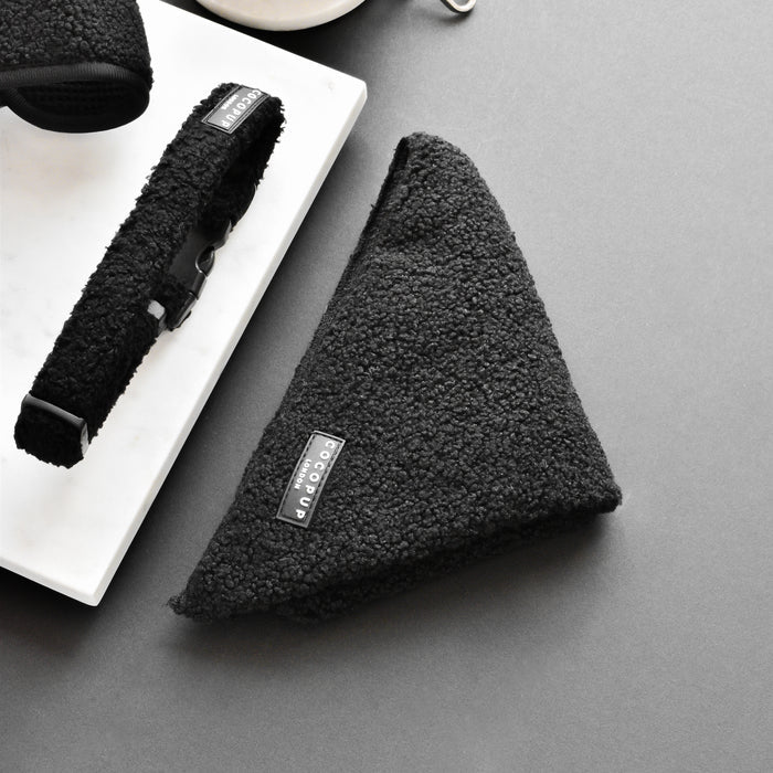 Black textured dog accessories on a dark surface, including a triangular Teddy Bandana - Baloo from the Cocopup London range, a collar, and a harness. The items feature tags with branding, positioned on a white marble slab.