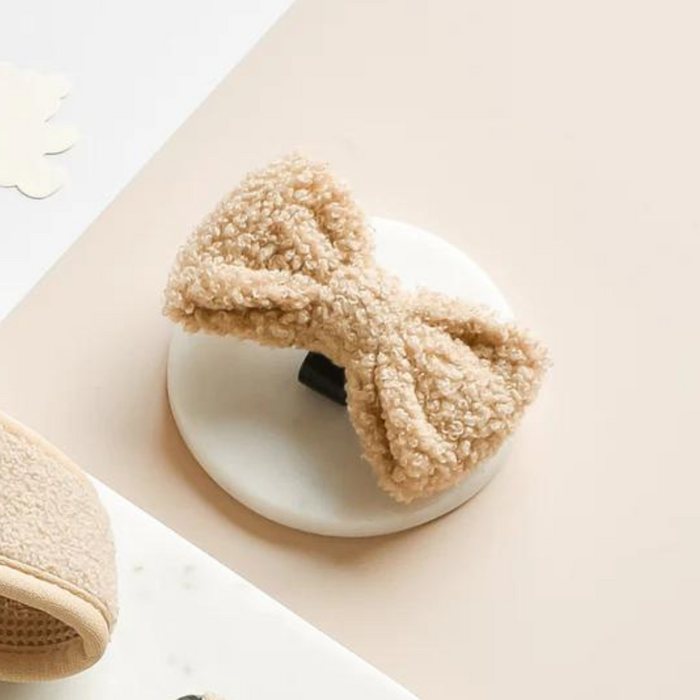 Beige Teddy Bow Tie hair clip by Cocopup London on a round white card, with fabric placed next to it.