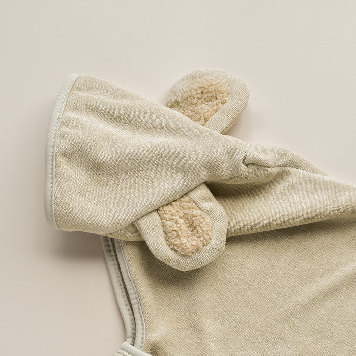 A close-up image of the Teddy Drying Robe by Cocopup London, featuring a soft, beige-colored fabric with sewn-on bunny ears. The inner side of the ears has a fluffy, cream-colored texture. Made from smooth and plush microfibre fabric, this garment offers a cozy appearance.