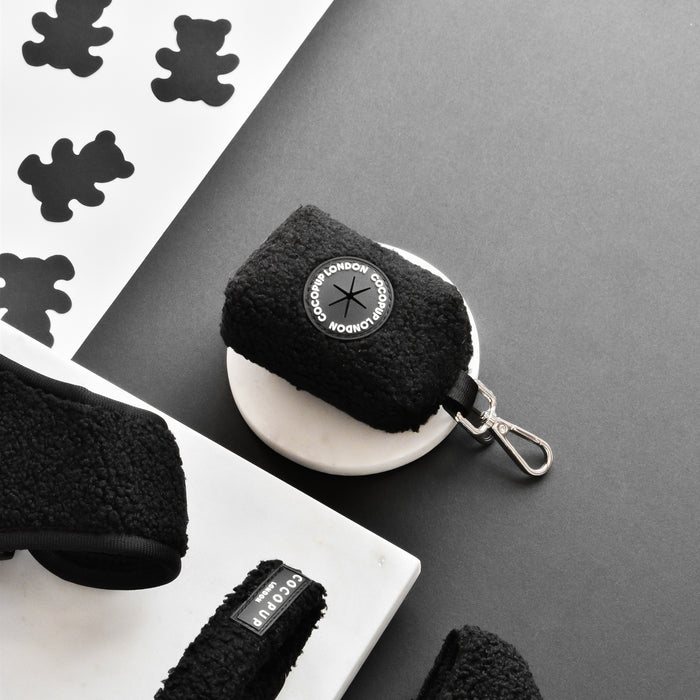 Brown teddy-textured poop bag holder with key clip on a dish, next to paper bear shapes.