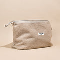 Beige teddy-style expandable makeup bag with front label, displayed on a neutral background.