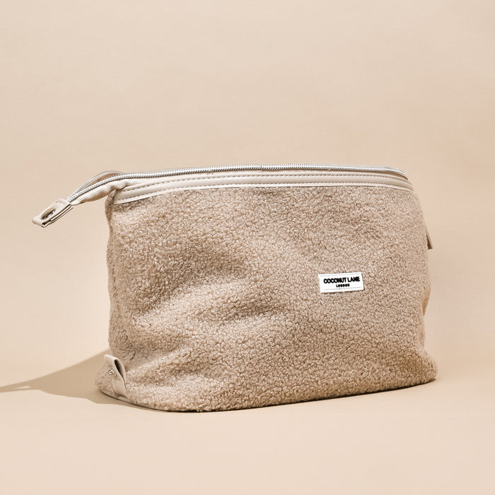Beige teddy-style expandable makeup bag with front label, displayed on a neutral background.