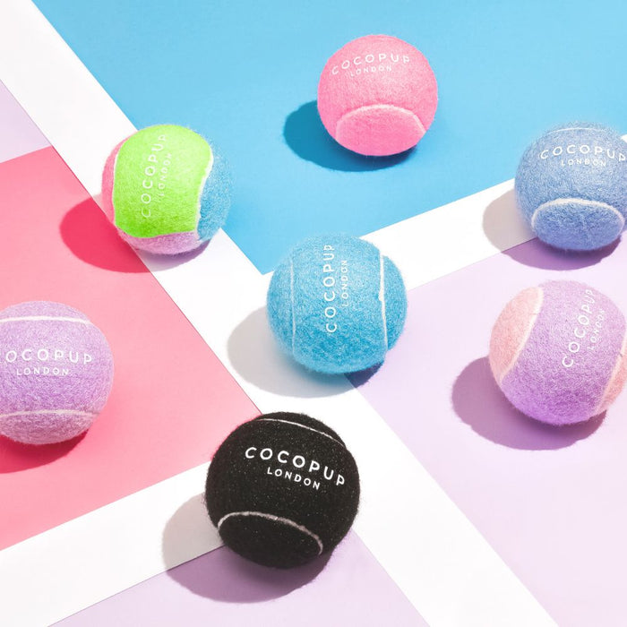 Seven blue Cocopup London tennis balls on a pastel geometric background.