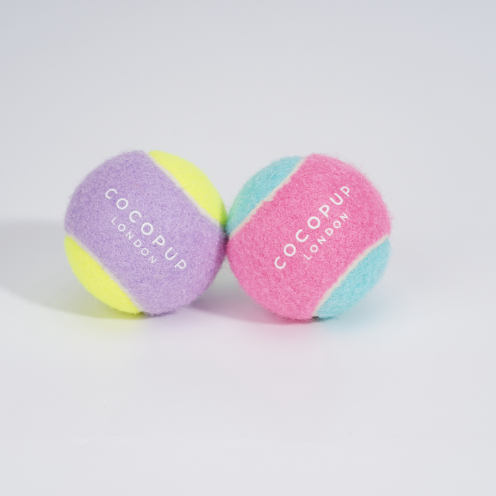 Two Cocopup London tennis balls, one lilac and one yellow, both with “Cocopup London” printed on the surface.