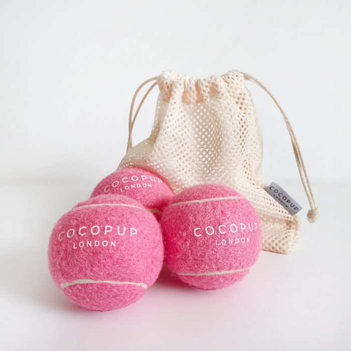 Three pink Cocopup London tennis balls with a cream mesh bag on a white background.